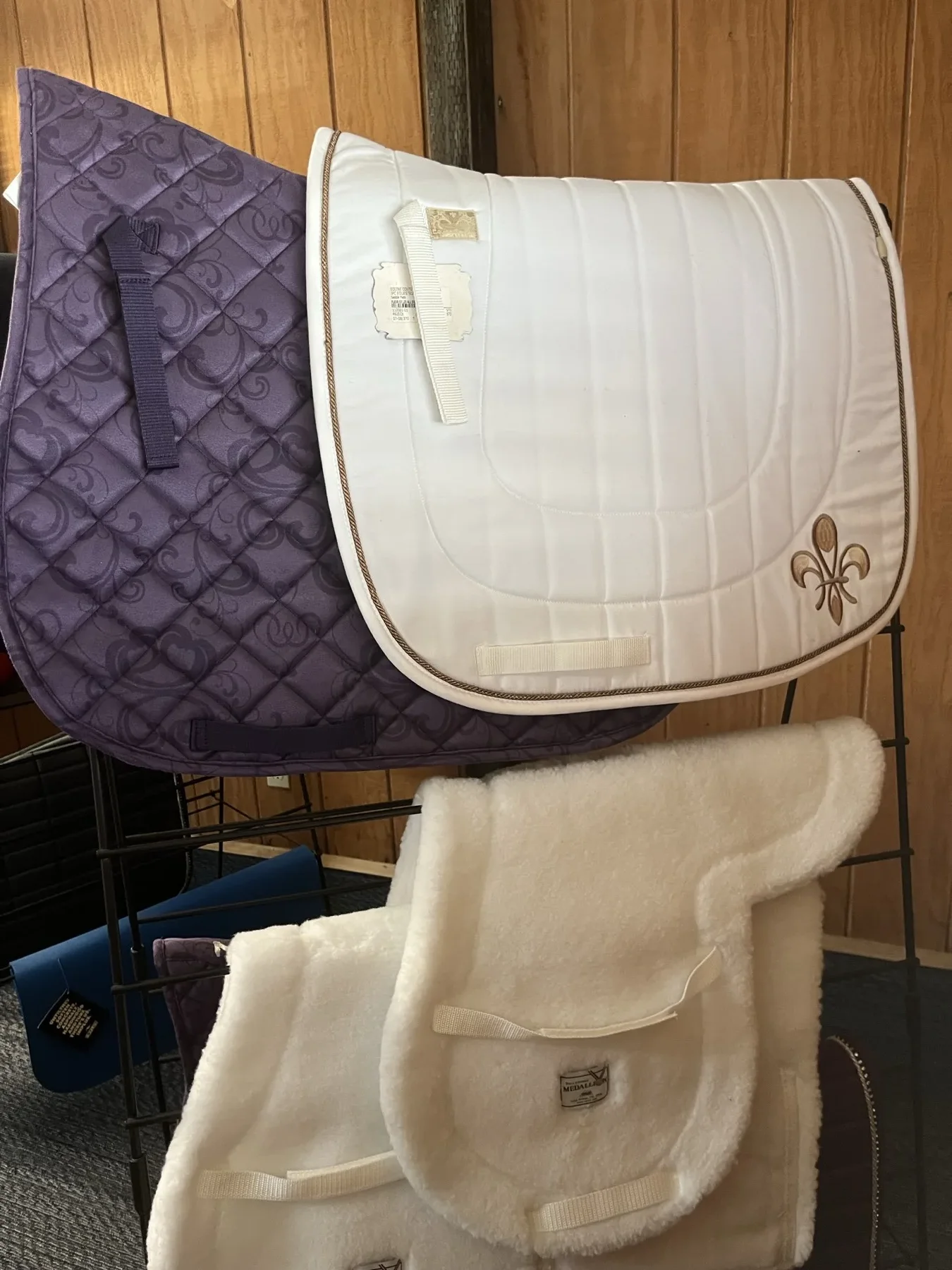 Quilted saddle pads and a sheepskin pad displayed on a tack room rack